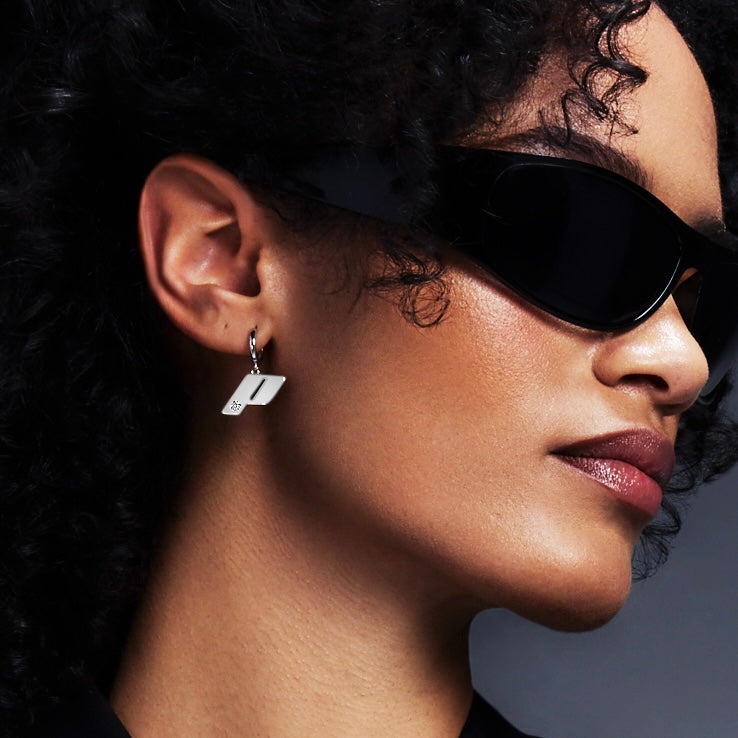 Close-up profile of model wearing Play's sterling silver Drop earring, styled with oversized black sunglasses against a gradient grey backdrop.