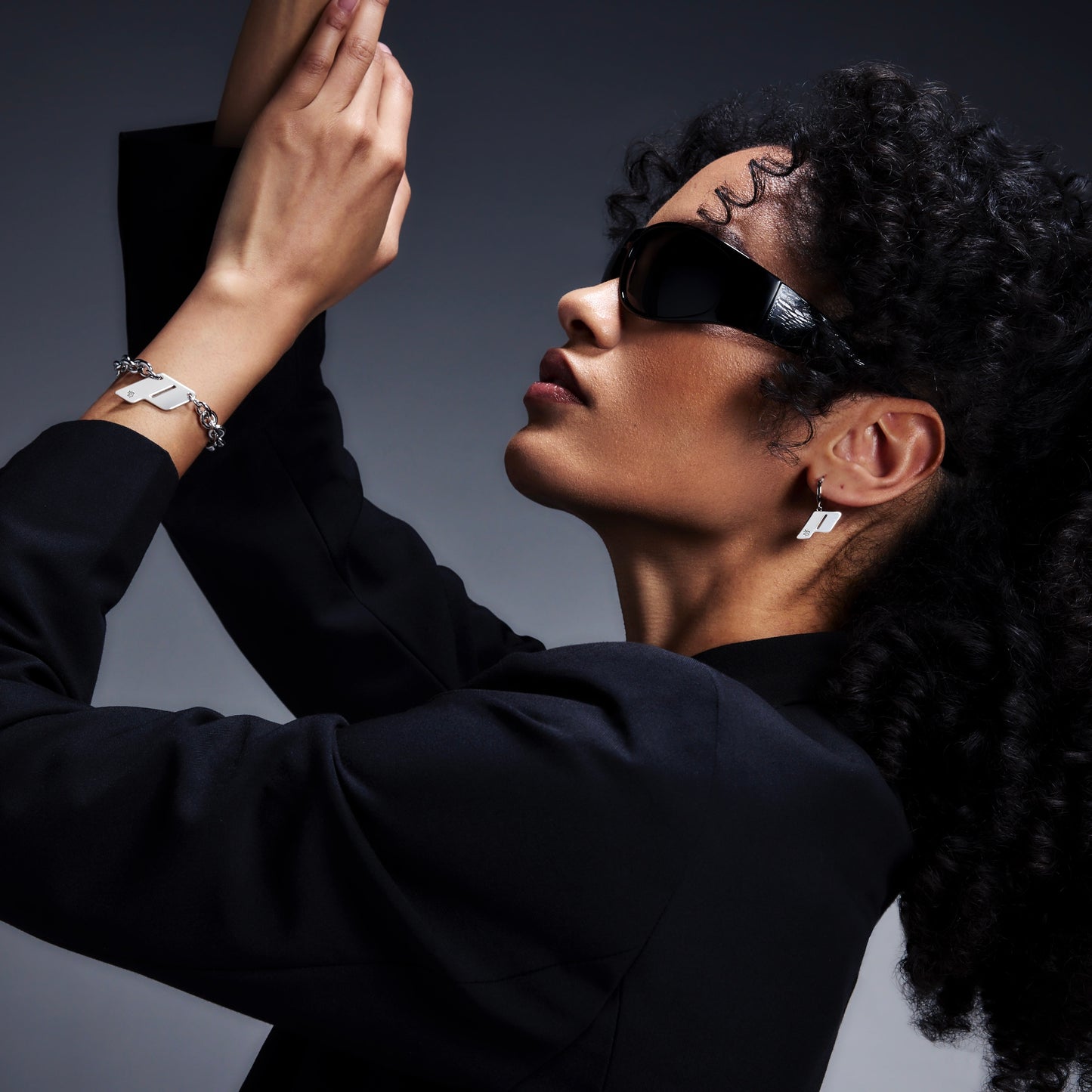 Model wearing Play's sterling silver Drop earrings, styled with sculptural black outfit against a gradient background.