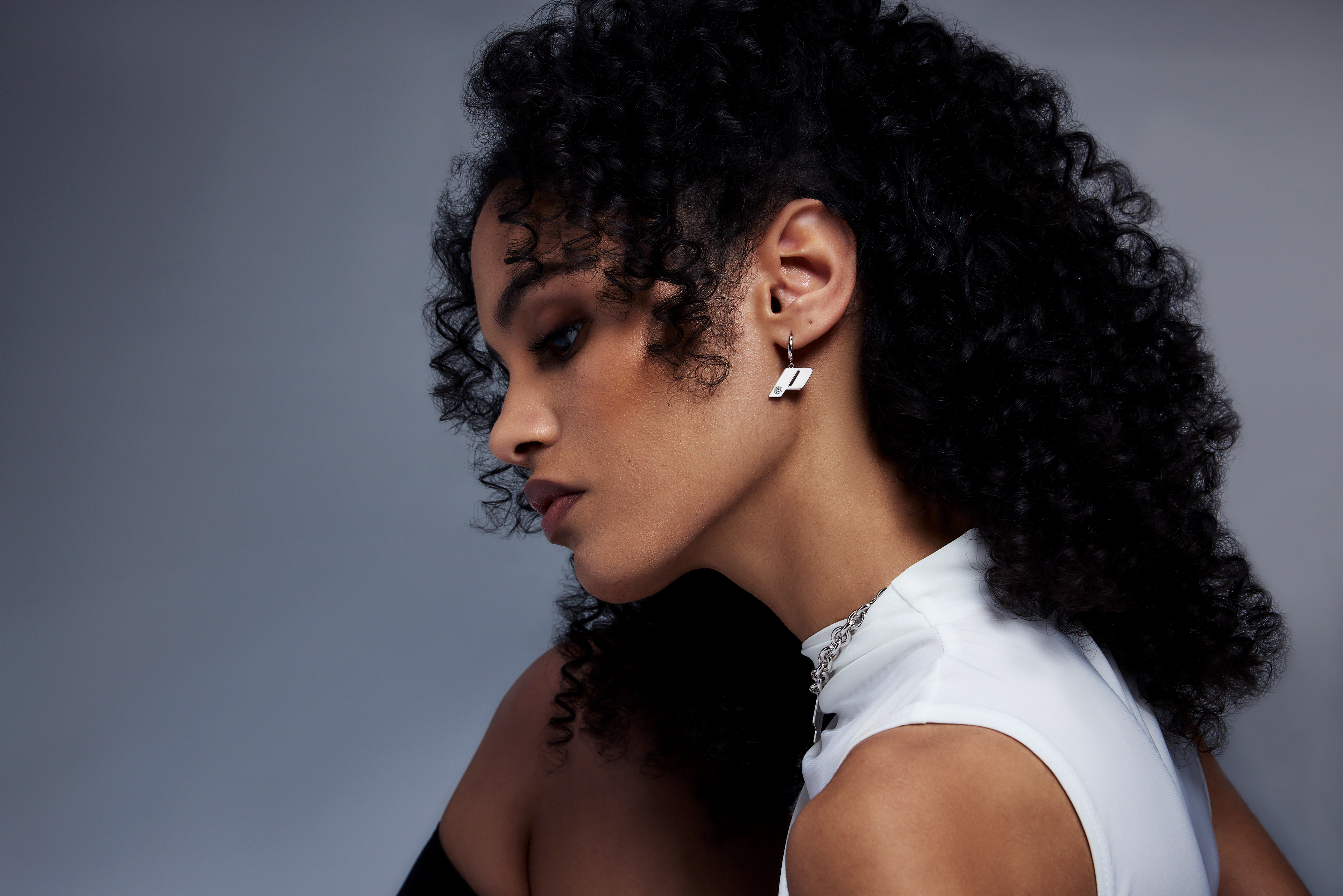Model with curly hair wearing Play drop earrings in sterling silver, photographed against a soft gradient backdrop.
