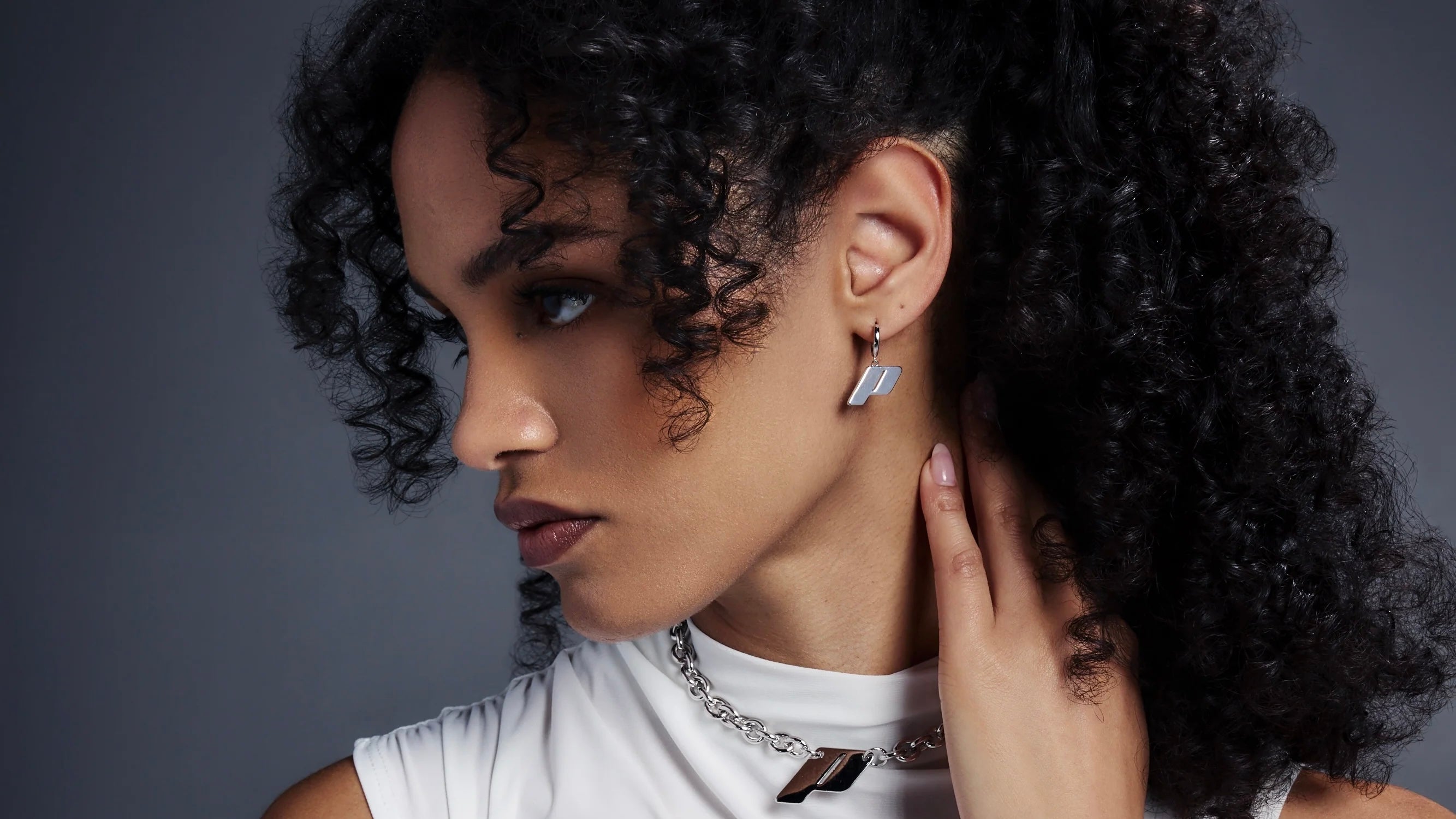 Model wearing Play drop earrings and the Play monogram pendant necklace, photographed against a dark gradient background.