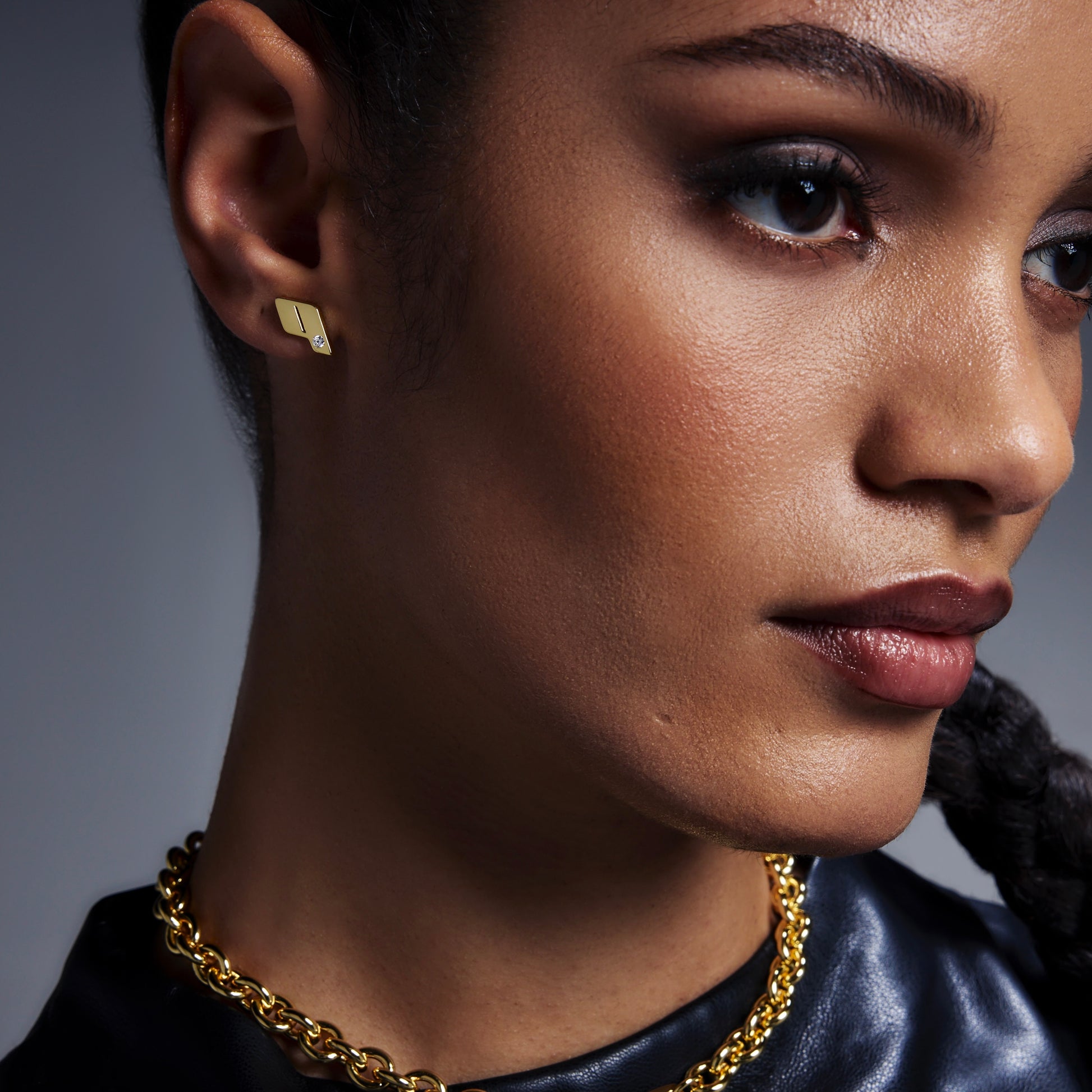 Close-up of a model wearing Play's 1§8k yellow gold monogram stud earrings and chain-link necklace, styled with a sleek back top.