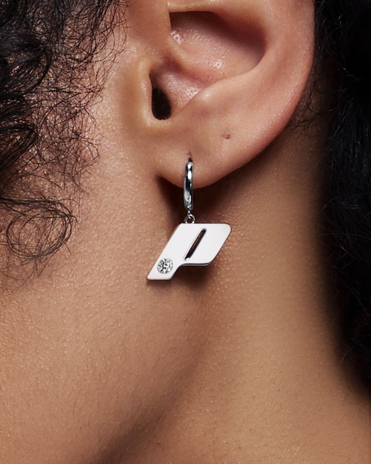 Close-up of a model wearing the Play monogram drop earring in sterling silver, featuring a natural diamond detail.
